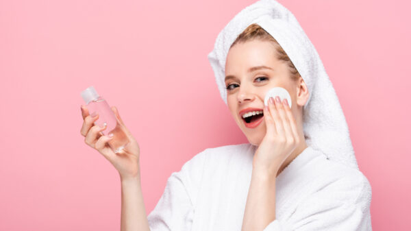 happy young woman in bathrobe with towel on head cleansing face with micellar water and cotton pad - Life Pharmacy Blog